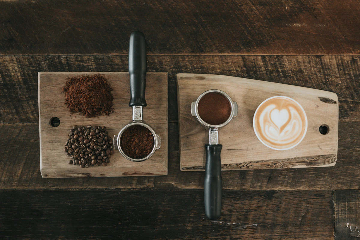Biji kopi, bubuk kopi, portafilter, dan secangkir latte di atas papan kayu